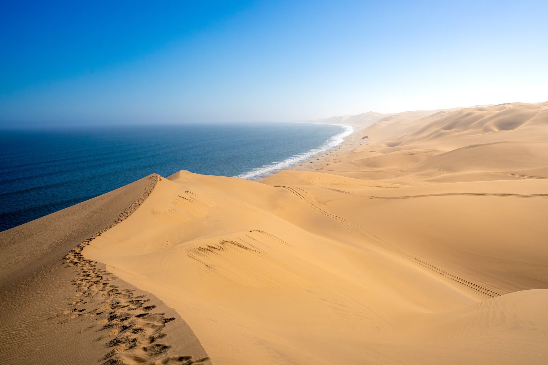 Panoramic view of desert sand dunes merging with the deep blue ocean