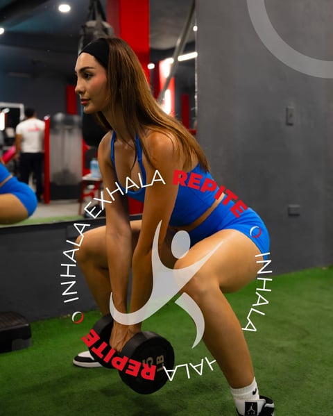 Woman in blue sports bra and shorts doing a squat exercise on green artificial turf in a modern gym with red and grey accents