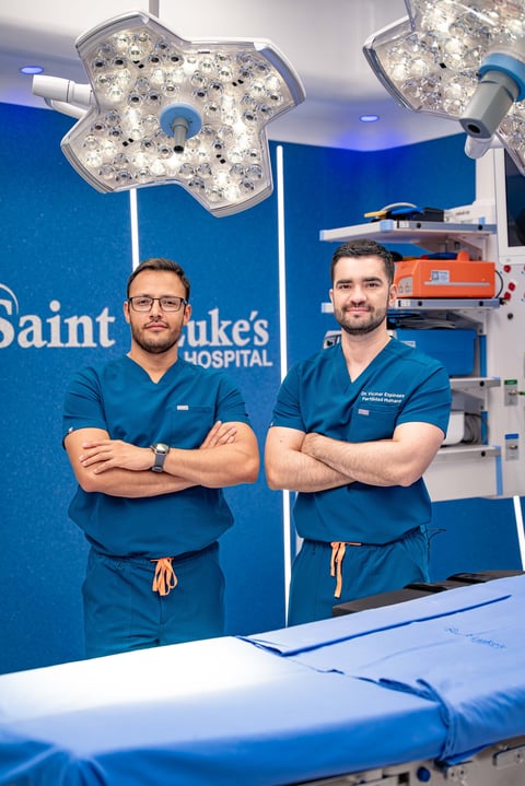 Two male surgeons in blue scrubs posing with crossed arms in an operating room at Saint Lukes Hospital