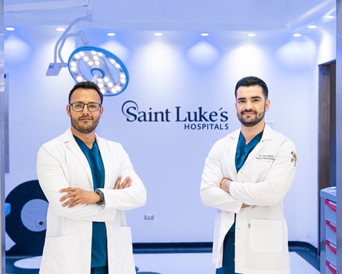 Two male doctors in white coats standing in a modern medical facility with Saint Lukes Hospitals branding and overhead surgical lighting visible
