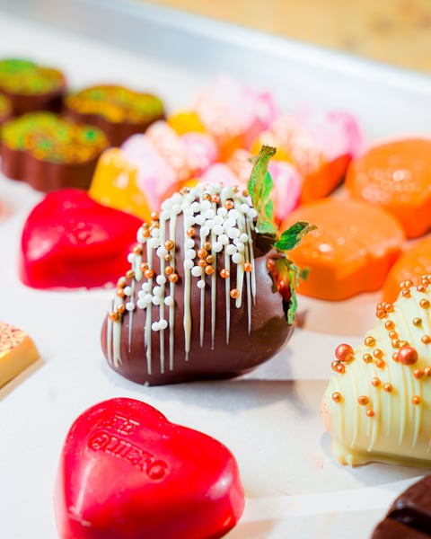 Chocolate-dipped strawberry with white drizzle and gold sprinkles among assorted decorated chocolates and candies